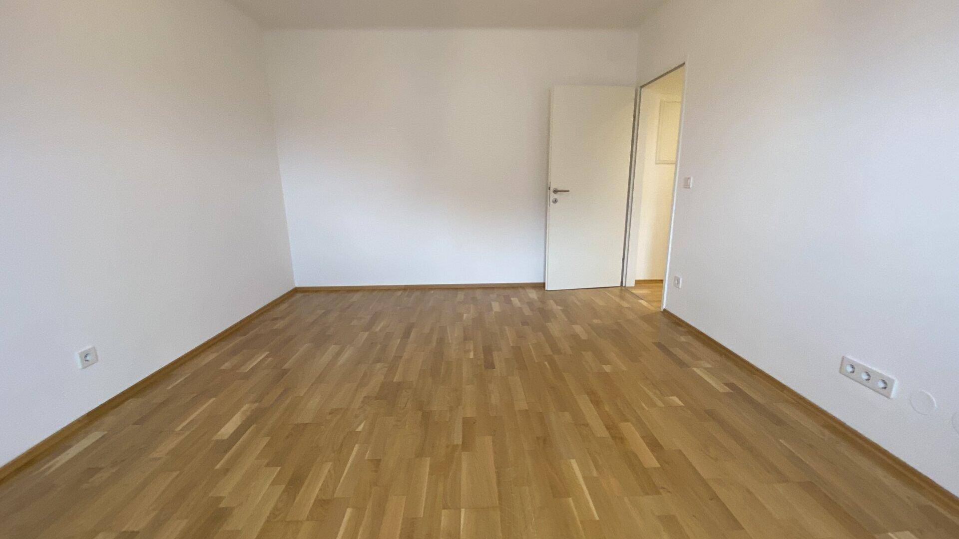 Leeres Zimmer mit hellem Holzparkettboden und weißen Wänden, bereit zur individuellen Gestaltung.