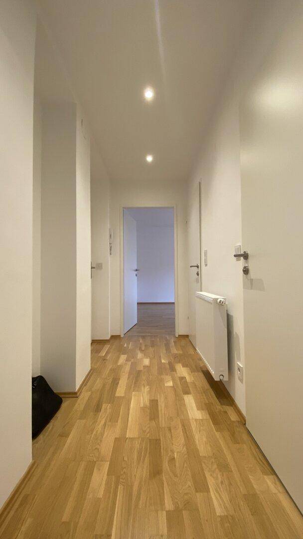 Langer, heller Flur mit Holzparkettboden und weißen Wänden, der verschiedene Bereiche verbindet.