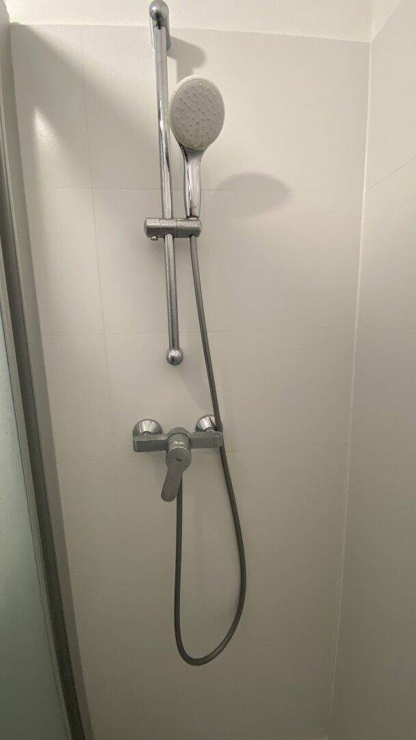Detaillierte Ansicht einer modernen Duscharmatur mit Handbrause in einem gefliesten Badezimmer.