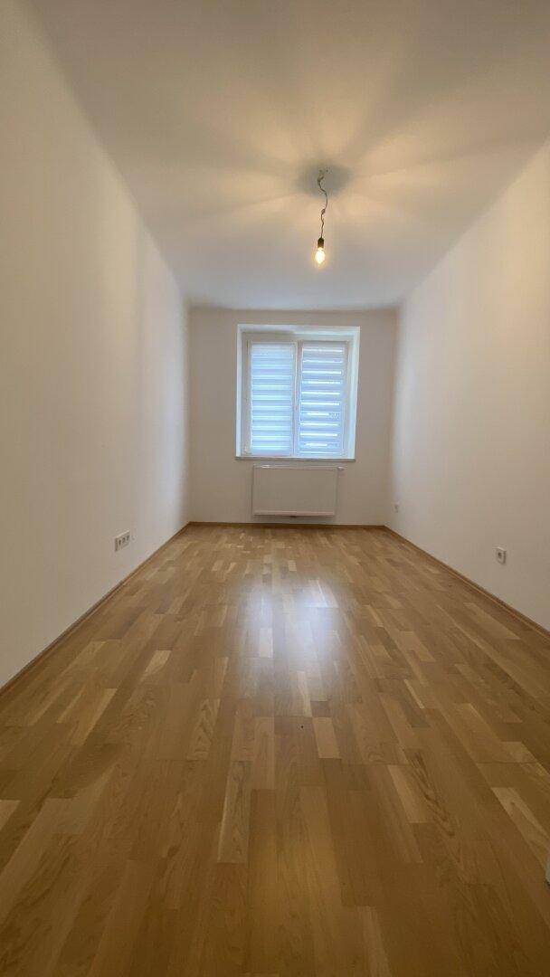 Helles Zimmer mit Holzparkettboden und Fenster mit Jalousien, ideal als Schlaf- oder Kinderzimmer.