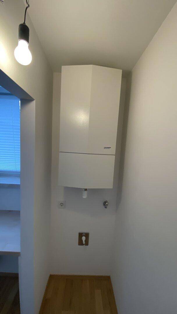 Kleiner Hauswirtschaftsraum mit wandmontierter Heizungsanlage und hellem Holzparkettboden.