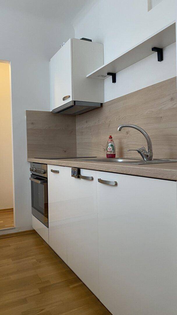 Moderne Küchenzeile mit weißen Schränken, Holzoptik-Arbeitsplatte und integrierten Geräten.