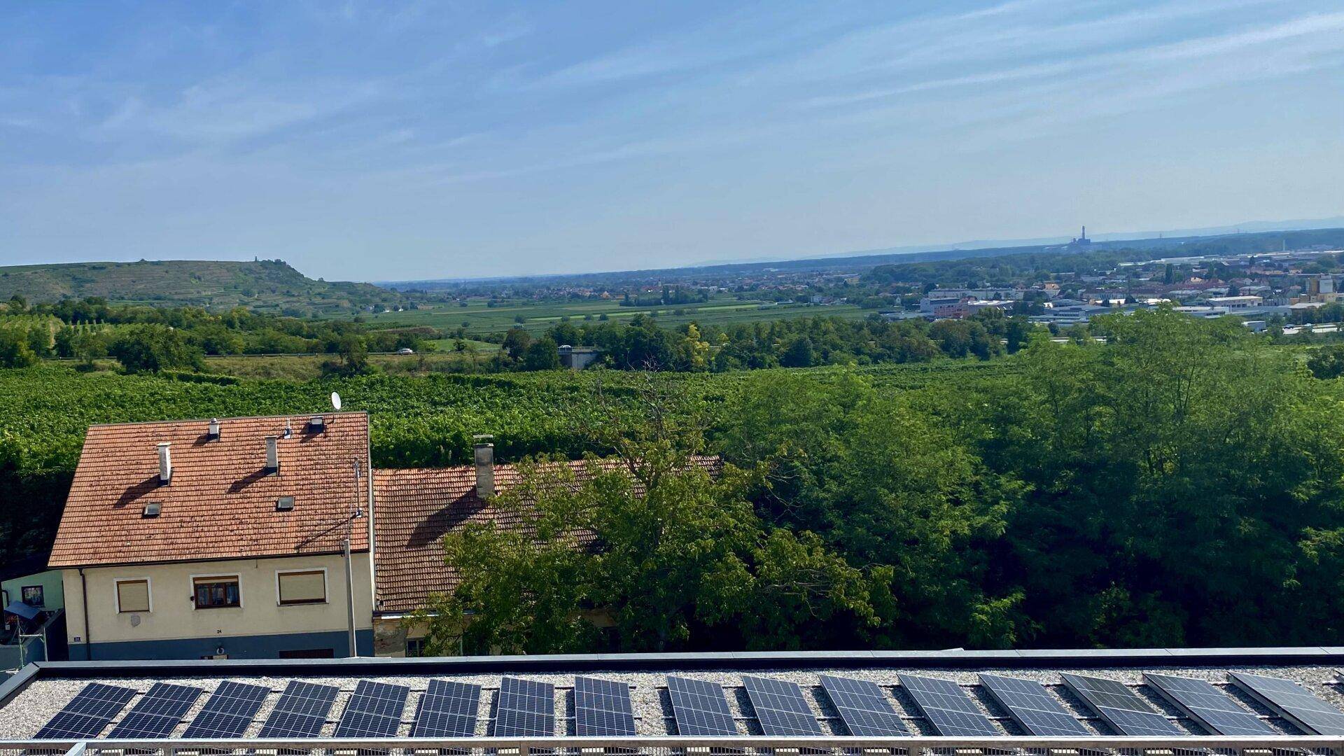 Dachfläche mit Photovoltaikanlage und weitem Blick über die grüne Landschaft und Stadt.