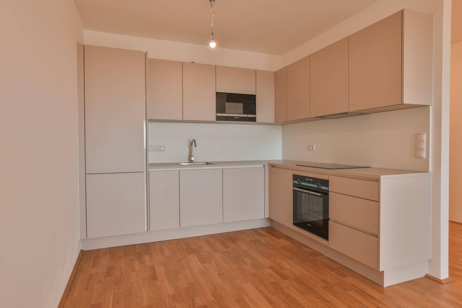 Voll ausgestattete, moderne Küche mit hellen Schränken, Backofen und Induktionskochfeld.
