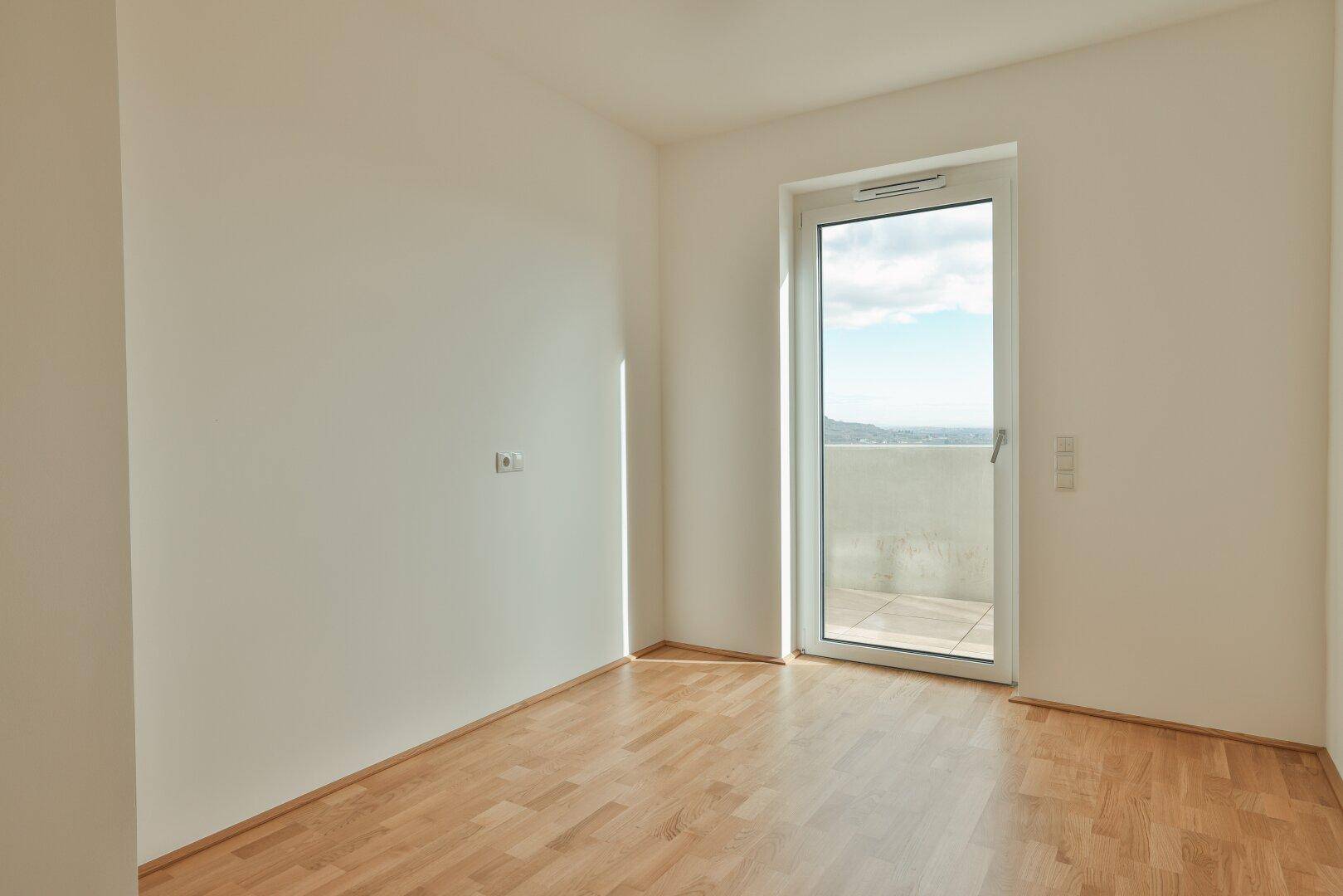 Helles Schlafzimmer mit Parkettboden und Balkonzugang, bietet einen weiten Ausblick.