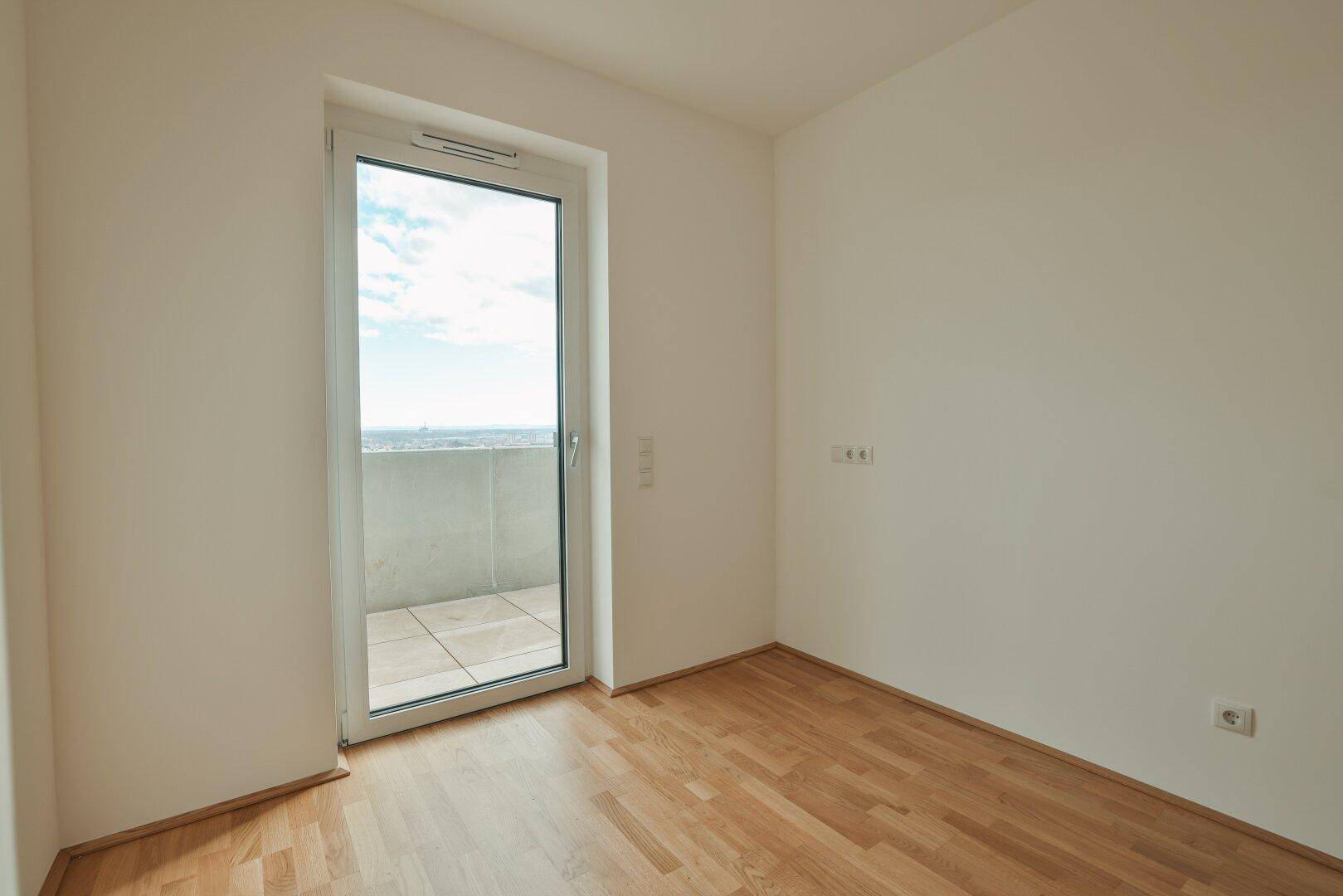 Schlafzimmer mit Parkettboden und Balkontür, die viel Tageslicht und frische Luft hereinlässt.