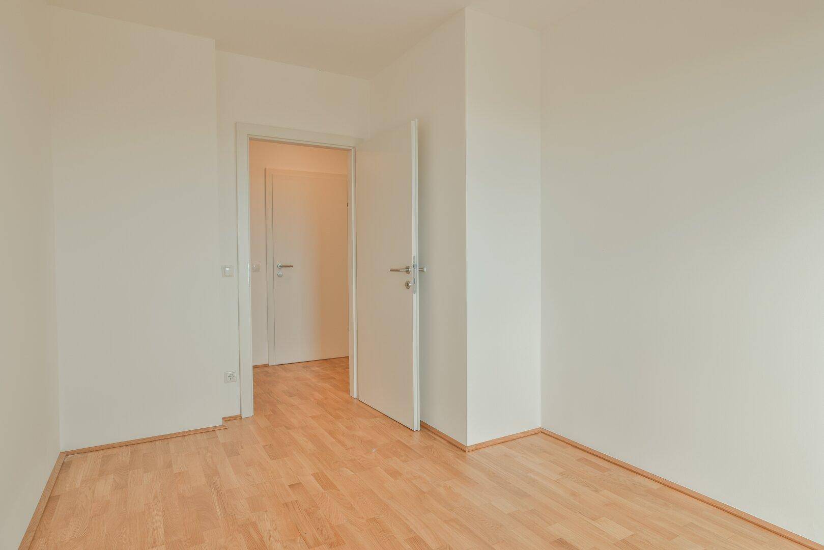 Helles Schlafzimmer mit Parkettboden und weißer Tür, bietet einen ruhigen Rückzugsort.