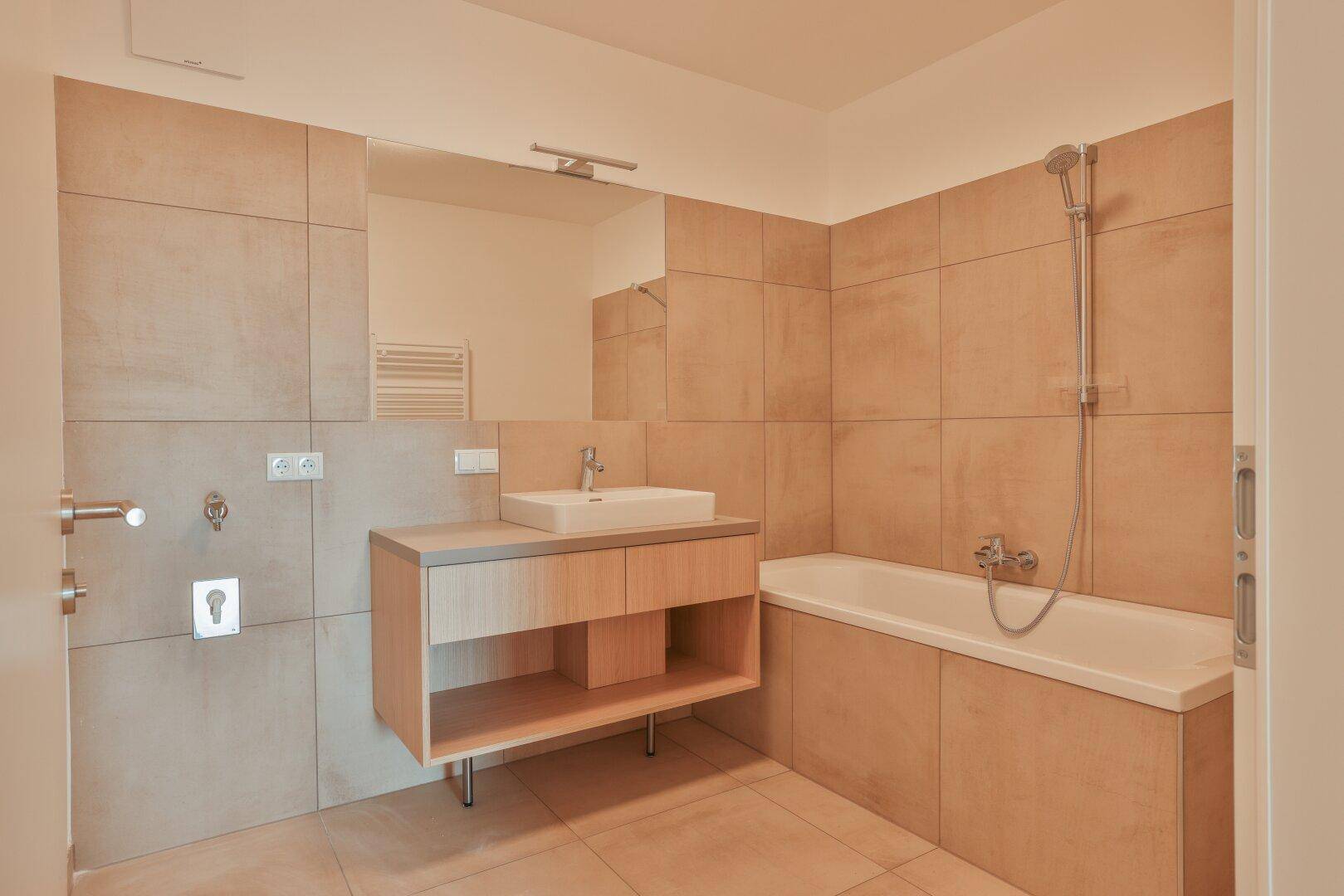 Modernes Badezimmer mit Badewanne, Waschtisch und beigefarbenen Fliesen, hell und funktional.