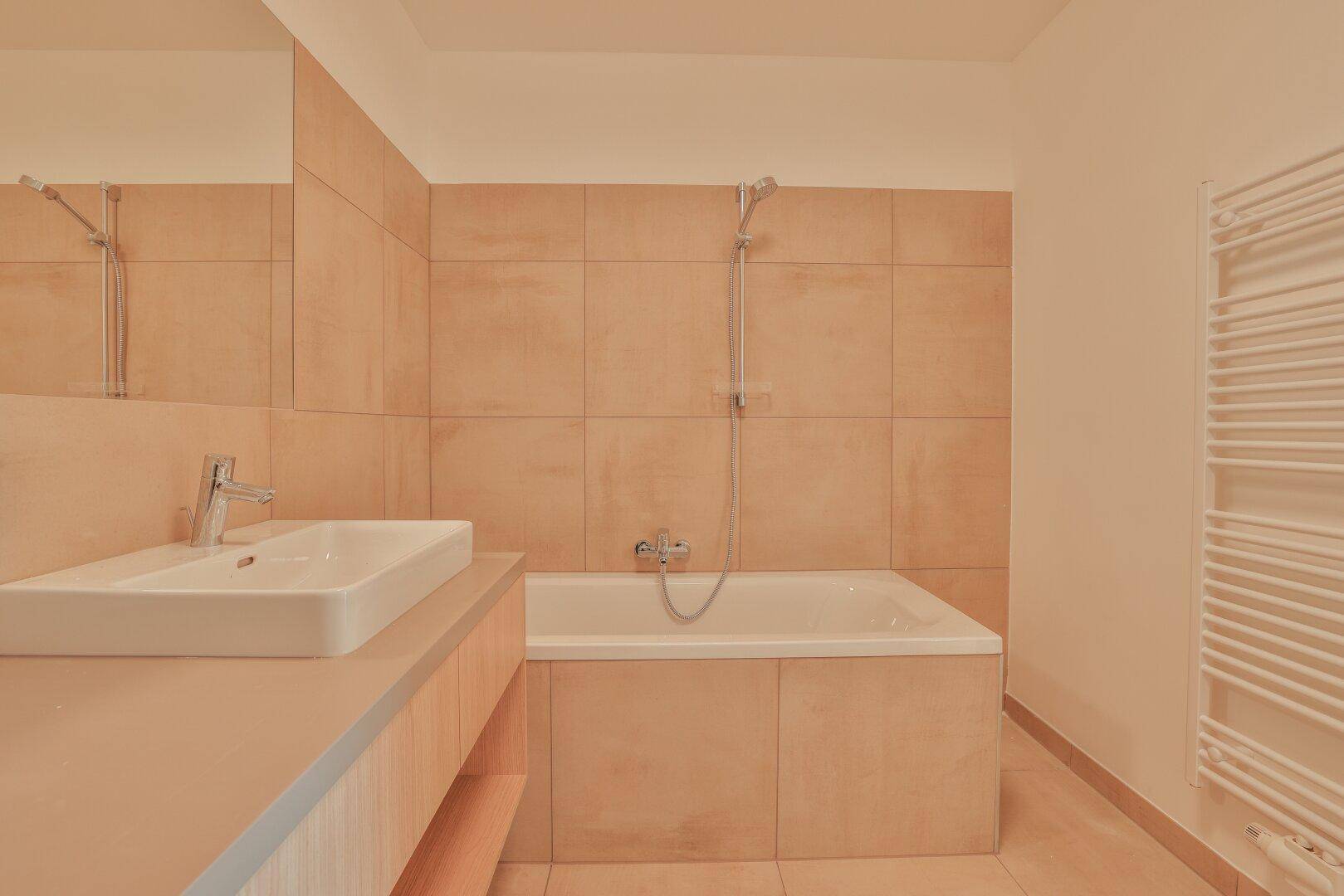 Modernes Badezimmer mit Badewanne, Waschtisch und beigefarbenen Fliesen, inklusive Handtuchheizkörper.