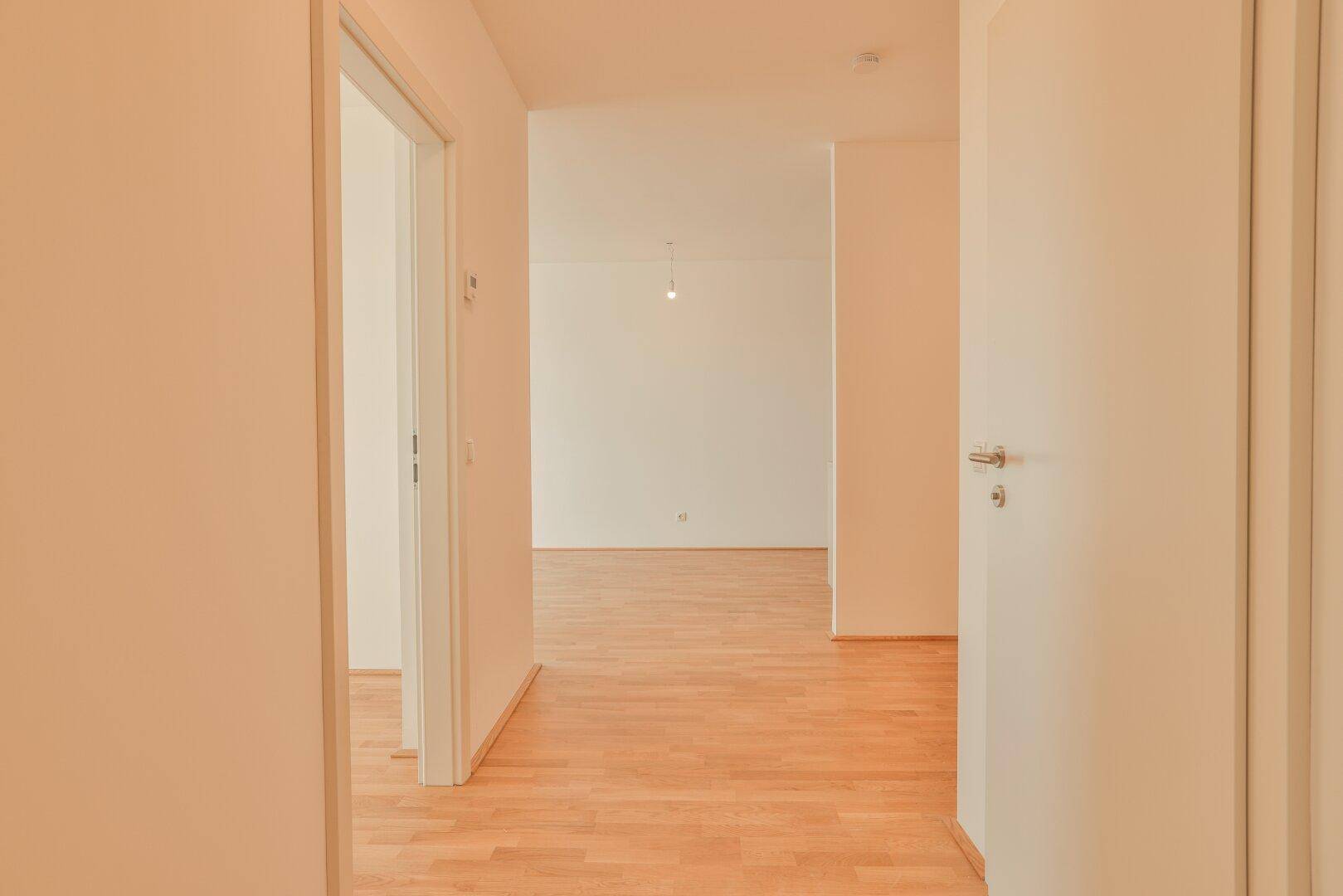 Langer, heller Flur mit Parkettboden, der zu verschiedenen Räumen der Wohnung führt.
