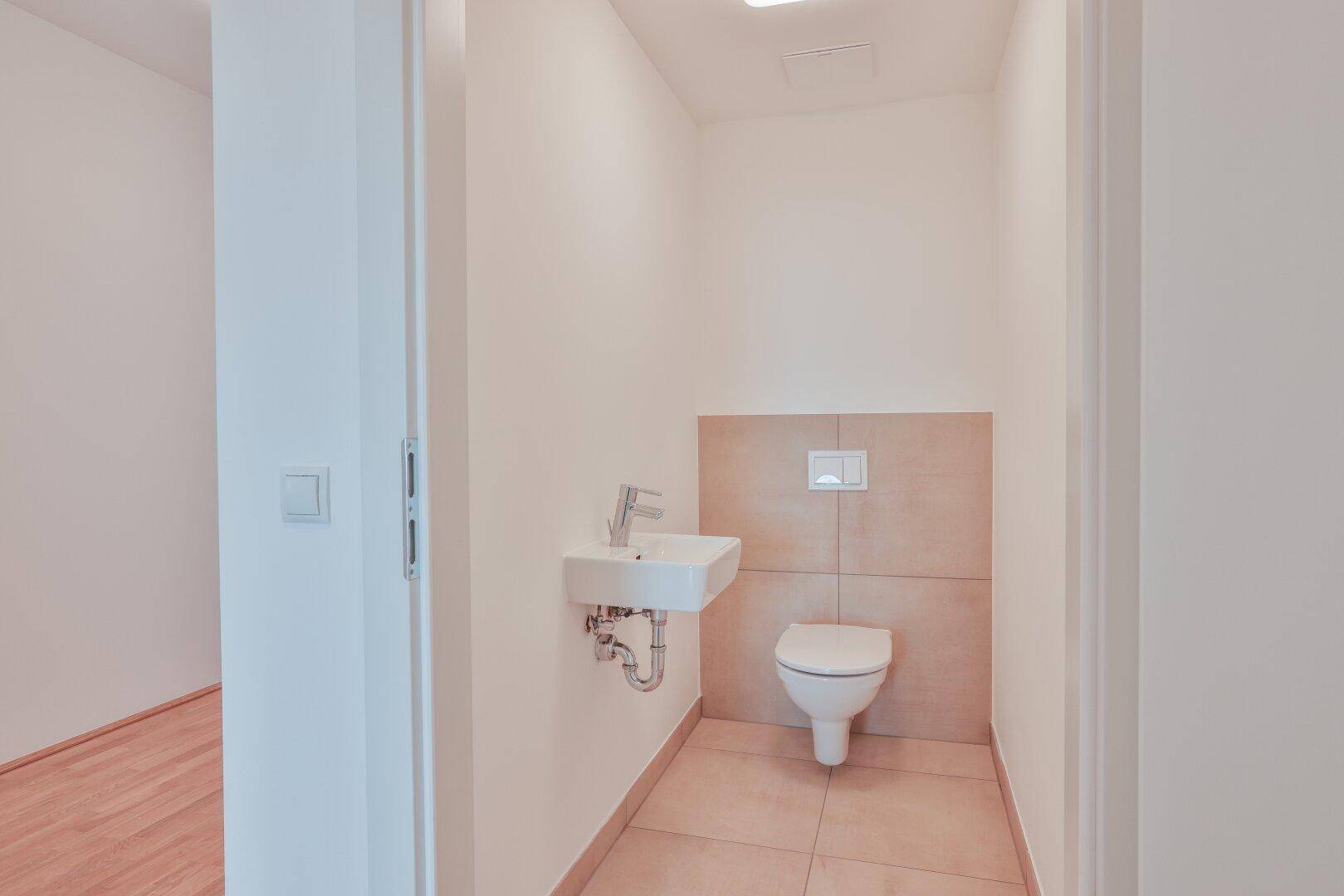 Modernes Gäste-WC mit wandhängender Toilette und kleinem Waschbecken, in hellen Tönen gehalten.