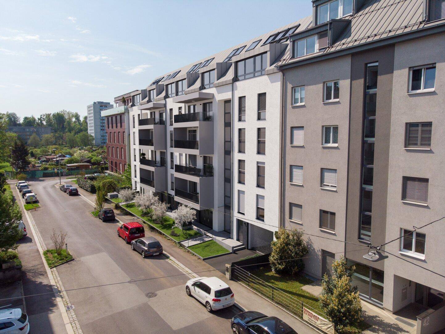 Luftaufnahme eines modernen Wohnkomplexes mit mehreren Gebäuden, Balkonen und Parkplätzen an der Straße.