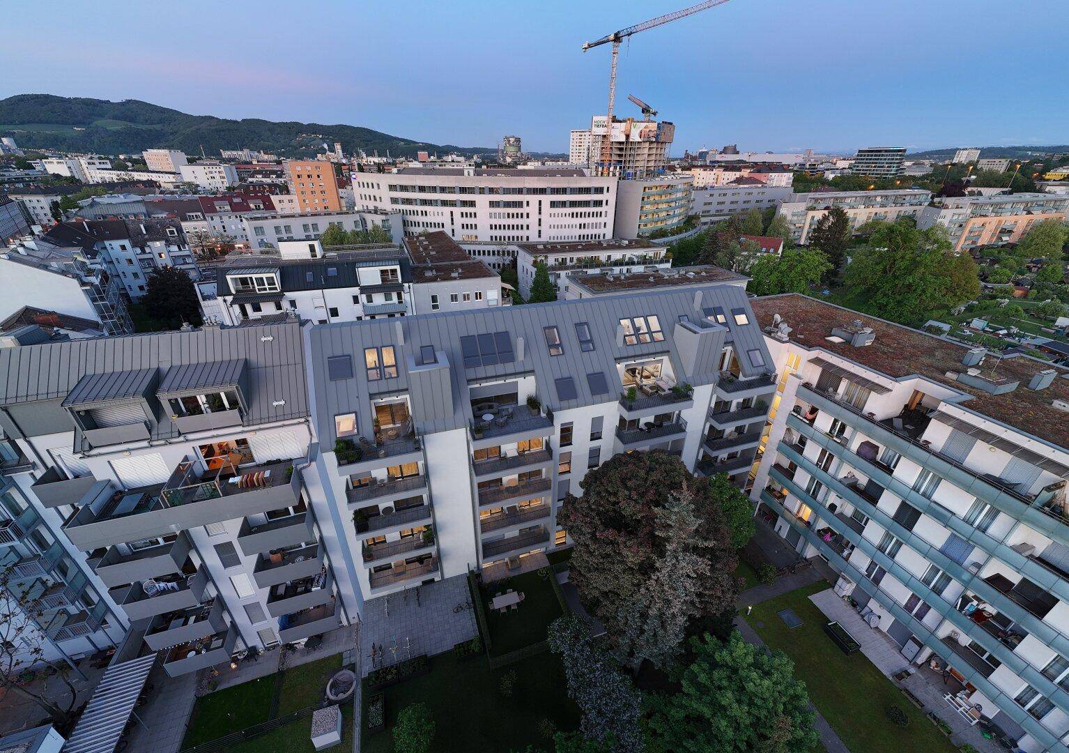 Weitläufige Luftaufnahme einer Stadtlandschaft mit Wohngebäuden und Bergen im Hintergrund.