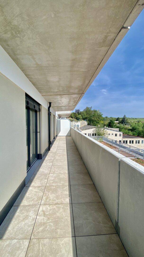 Heller Balkon mit Fliesenboden und weitem Blick auf die umliegenden Gebäude und Natur.