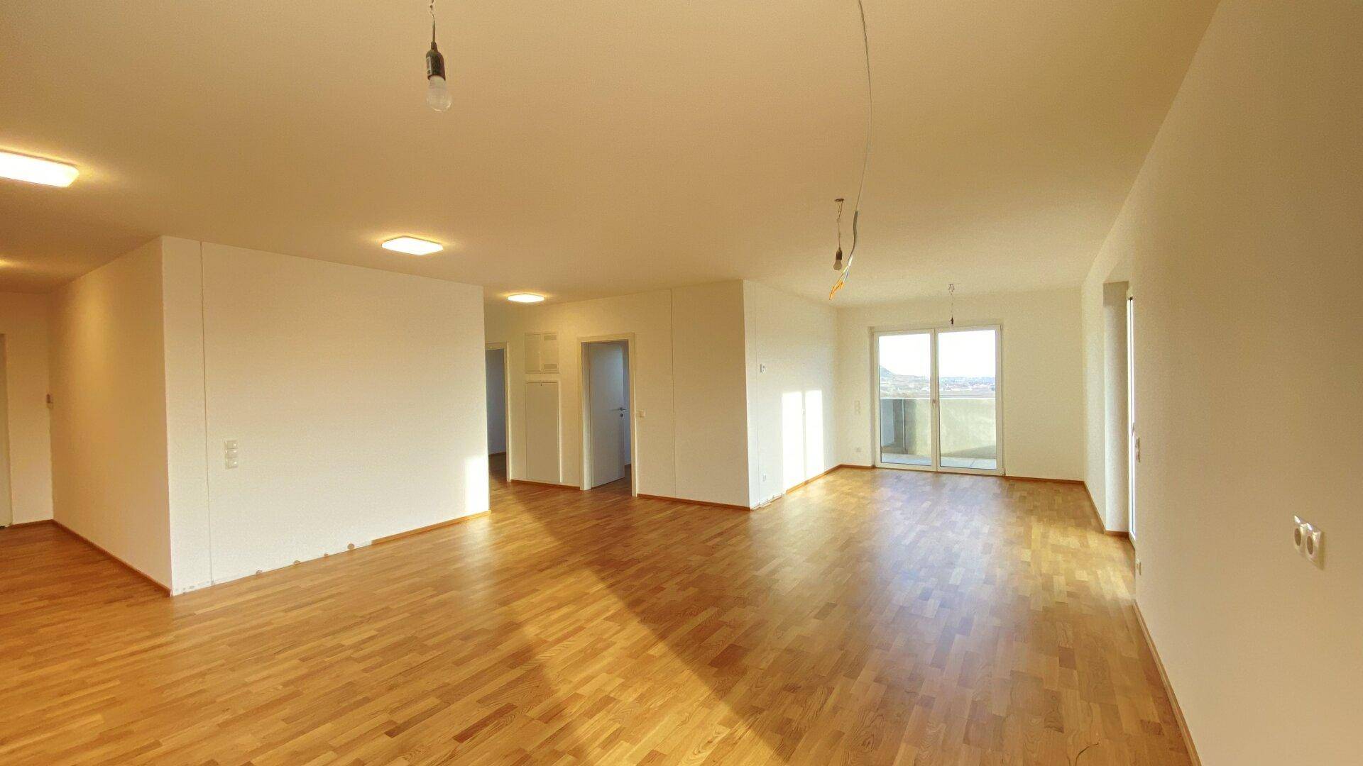 Helles Wohnzimmer mit Holzparkettboden und Zugang zu einem Balkon.