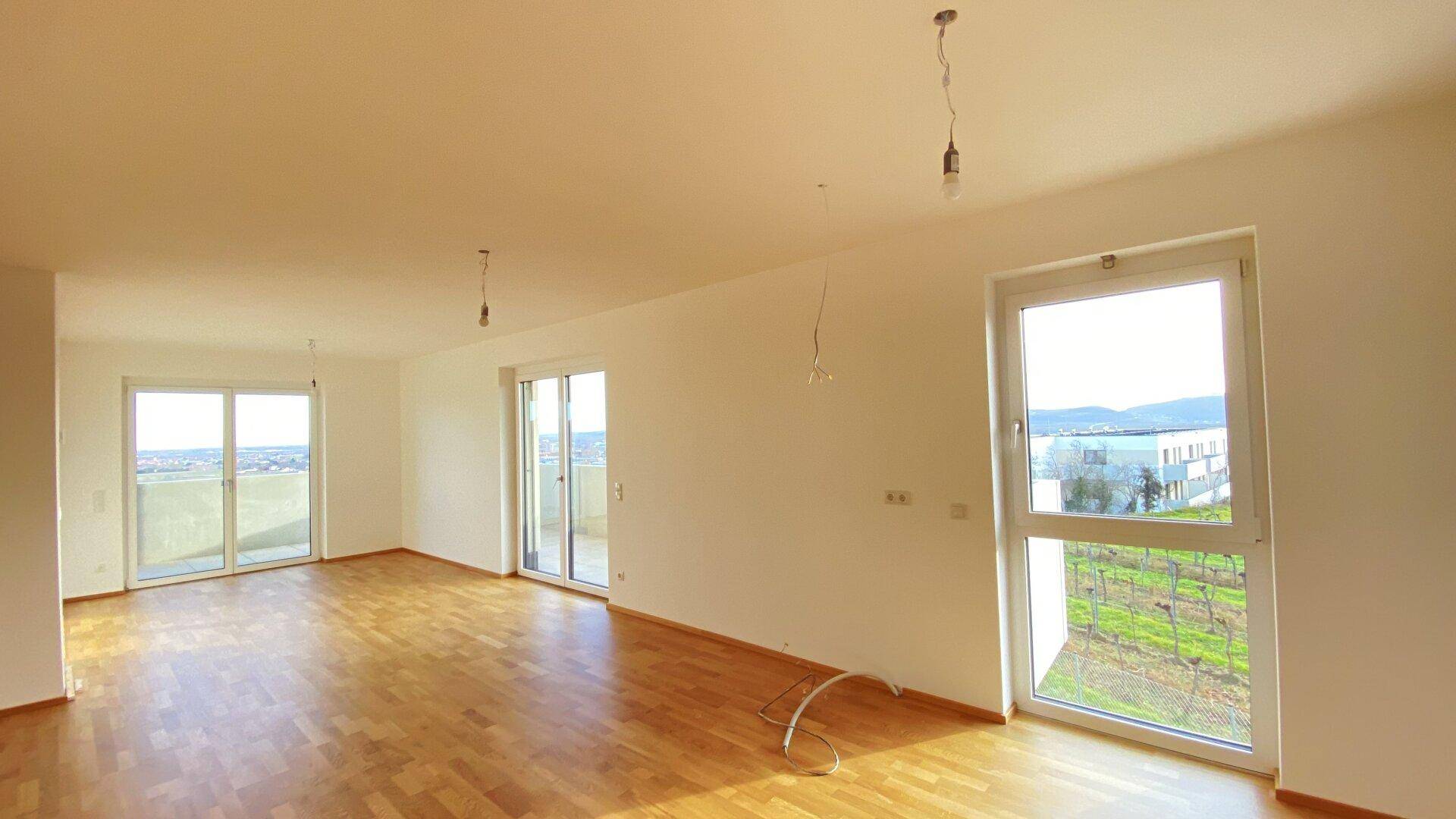 Geräumiges Wohnzimmer mit Holzparkettboden und großen Fenstern für viel Tageslicht.