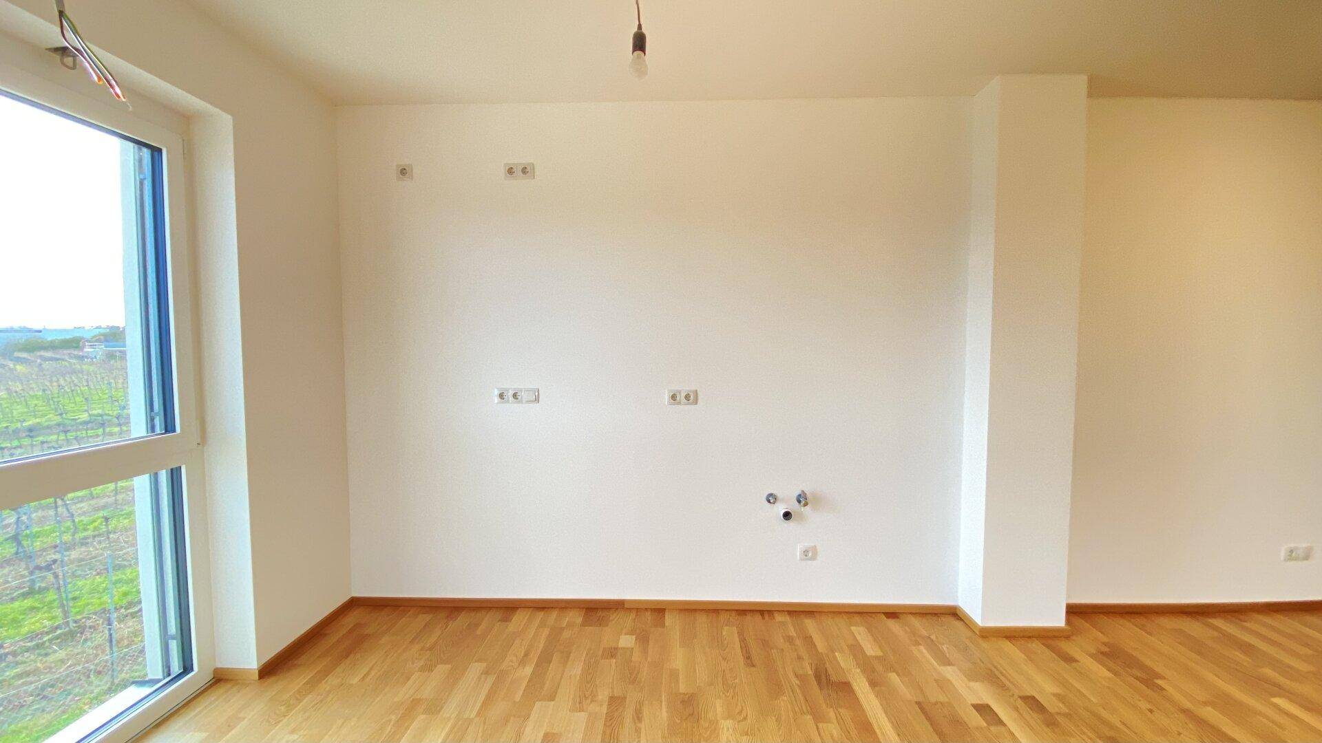 Heller Küchenbereich mit Holzparkettboden und Anschlussmöglichkeiten für Geräte.