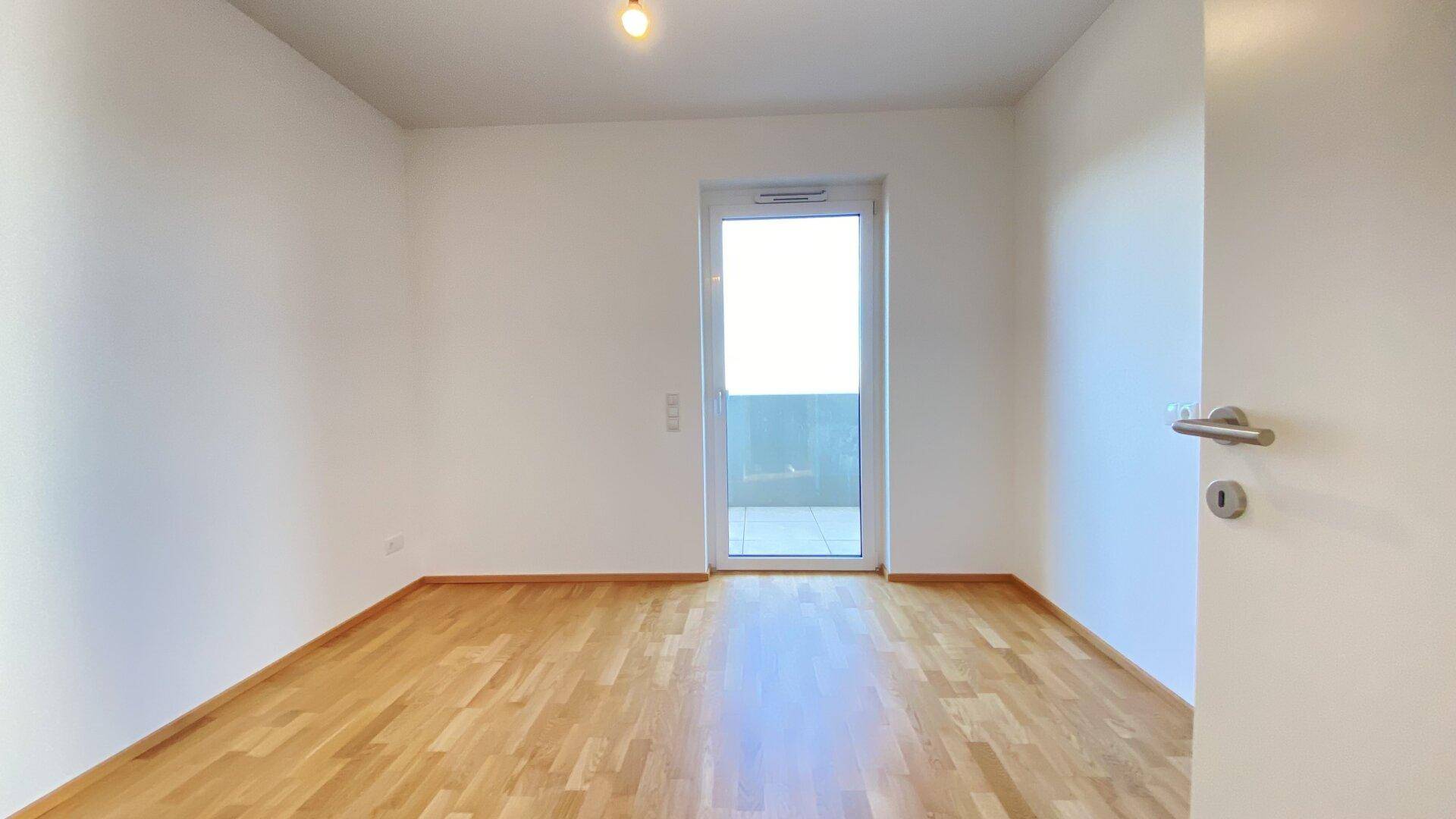 Geräumiges Schlafzimmer mit Holzparkettboden und Fenster für viel Tageslicht.