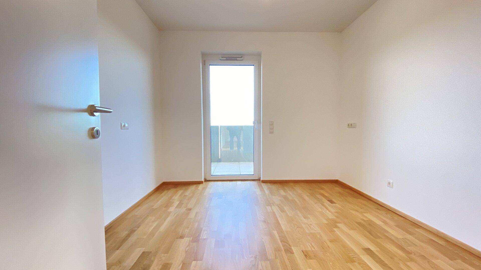 Helles Schlafzimmer mit Holzparkettboden und Zugang zu einem Balkon.