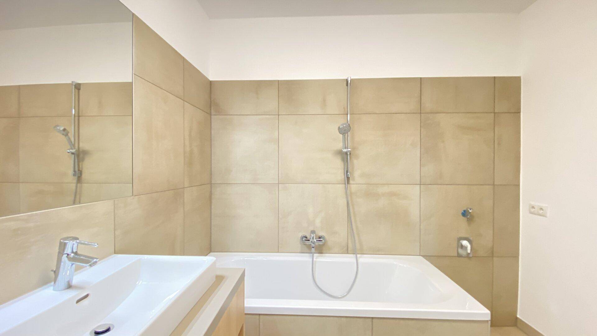 Helles Badezimmer mit beigefarbenen Fliesen, Badewanne und modernem Waschtisch.