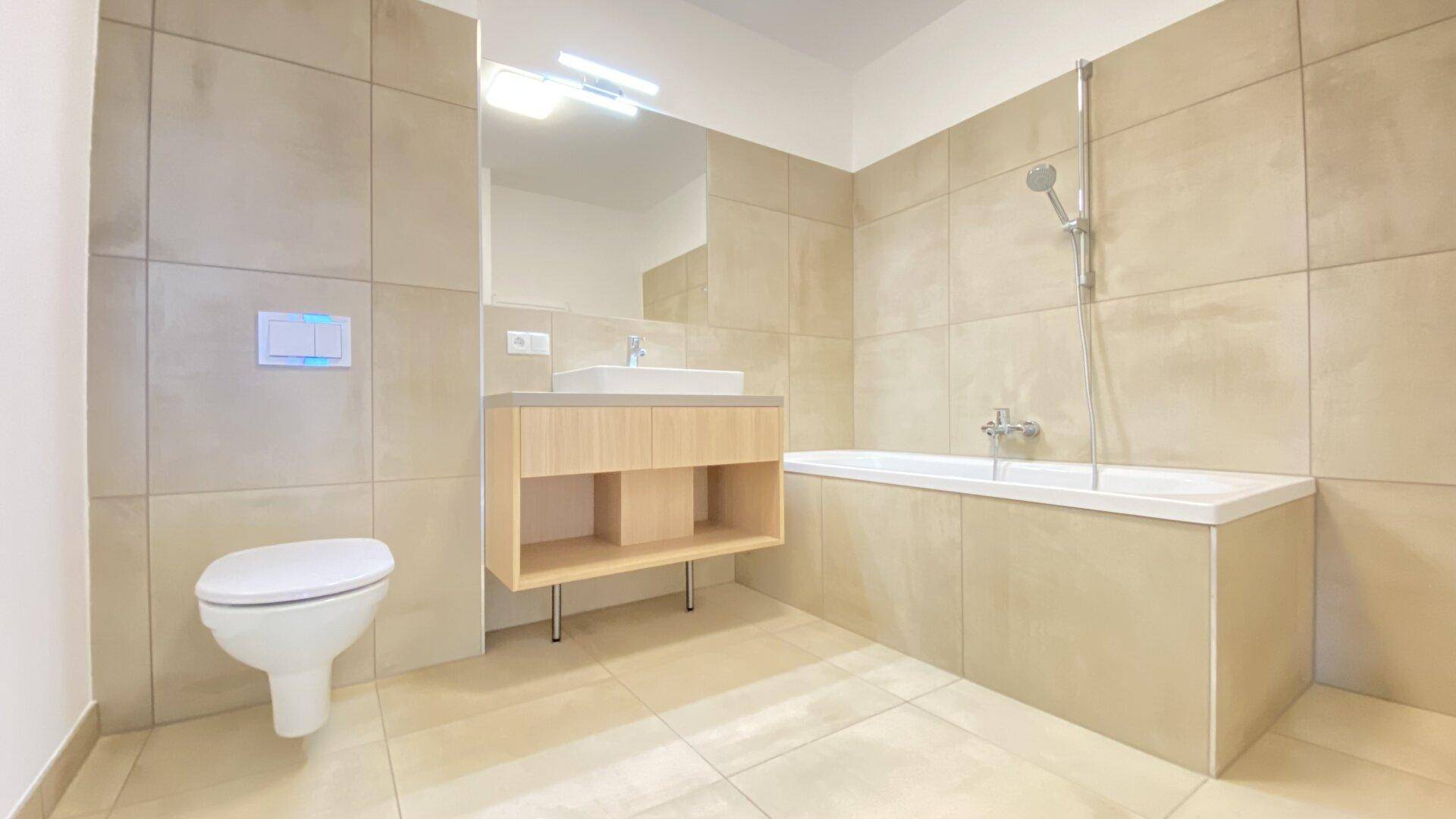 Modernes Badezimmer mit beigefarbenen Fliesen, Badewanne, WC und Waschtisch.