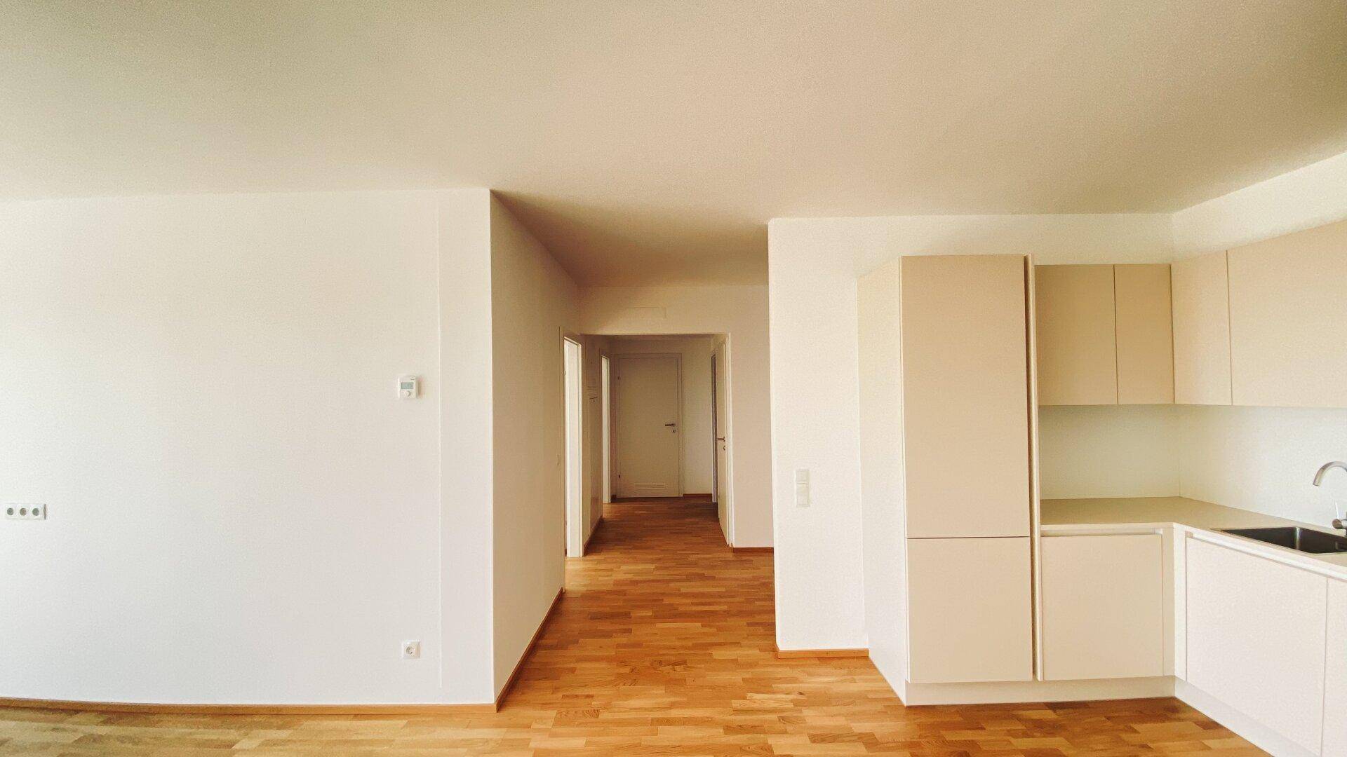 Heller Flurbereich mit Parkettboden, der zu weiteren Räumen führt, mit Blick auf eine Küchenzeile.