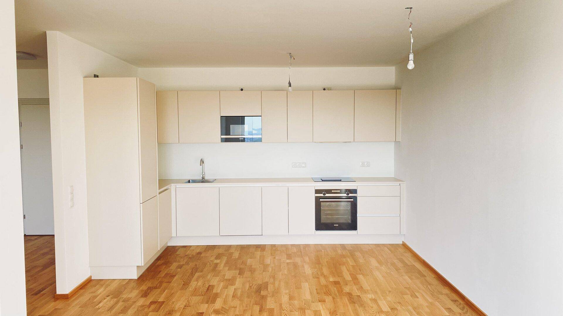 Moderne Einbauküche in hellem Design mit integrierten Geräten und Parkettboden, offen gestaltet.