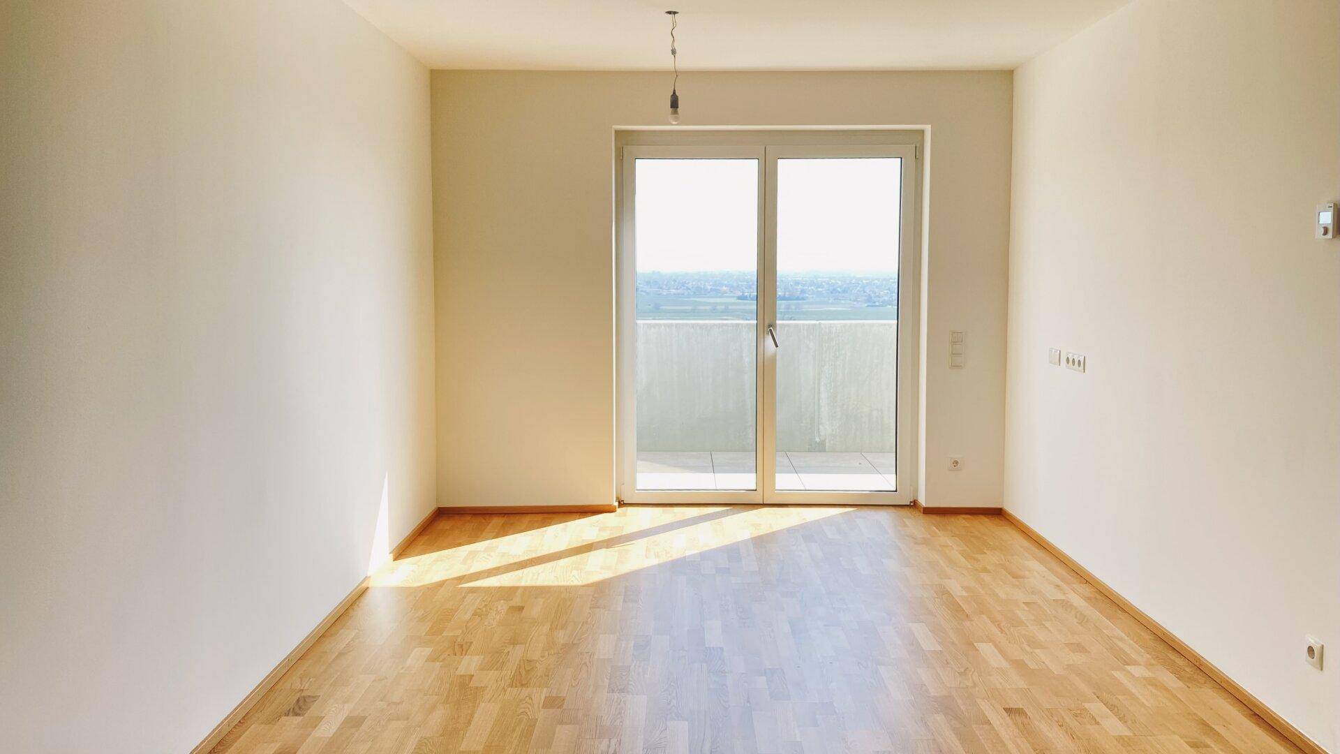 Heller, leerer Raum mit Parkettboden und Zugang zu einem Balkon, ideal für Wohn- oder Schlafzimmer.