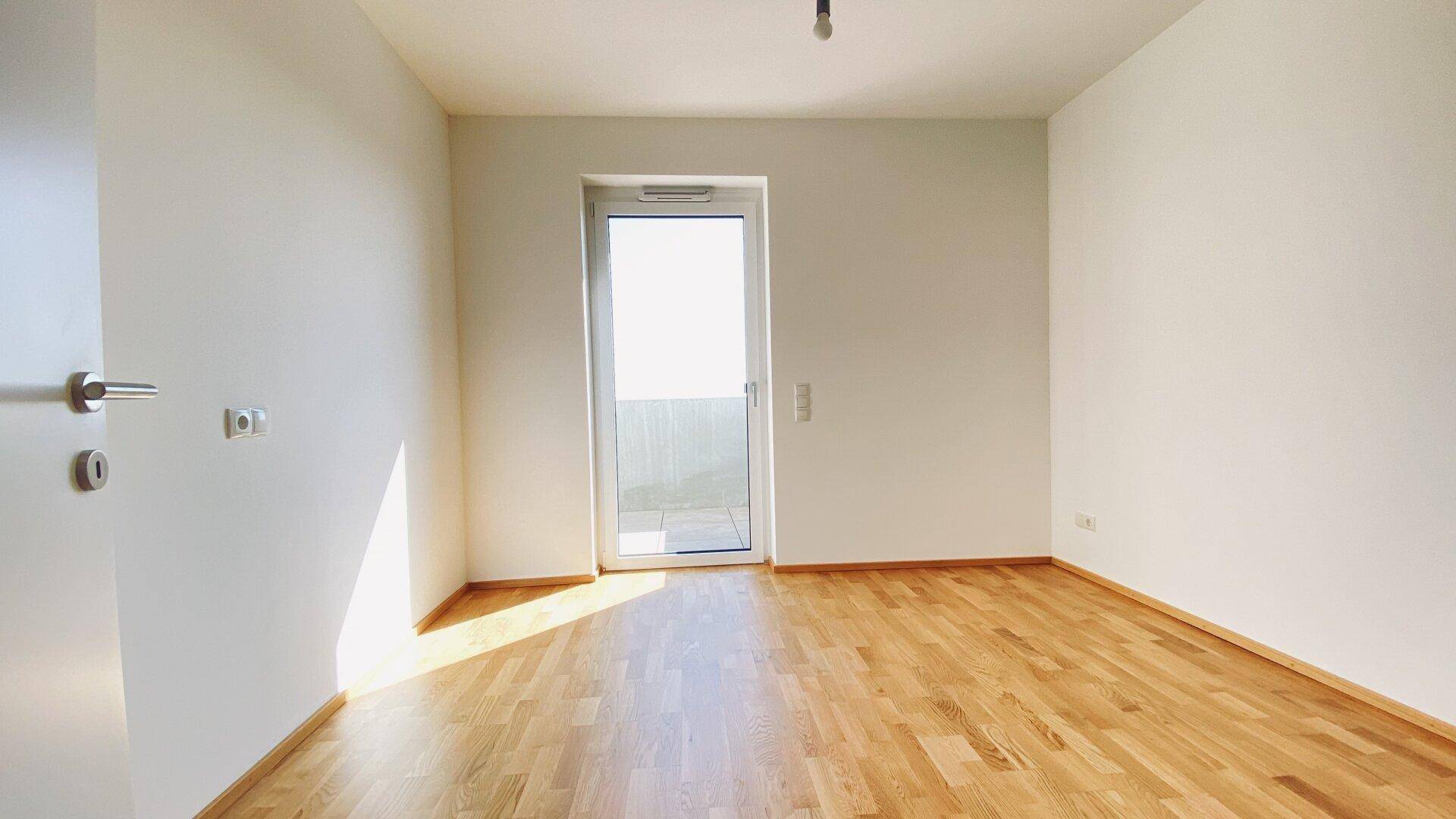 Lichtdurchfluteter Raum mit Holzboden und Zugang zu einem Außenbereich, bereit zur individuellen Gestaltung.