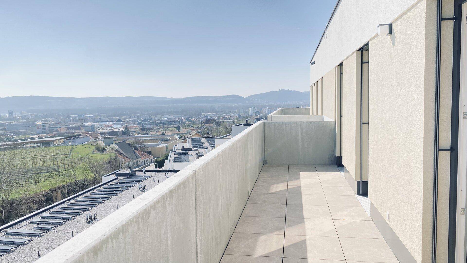 Langer Balkon mit Fliesenboden und weitem Blick über die Stadt und die umliegende Landschaft.