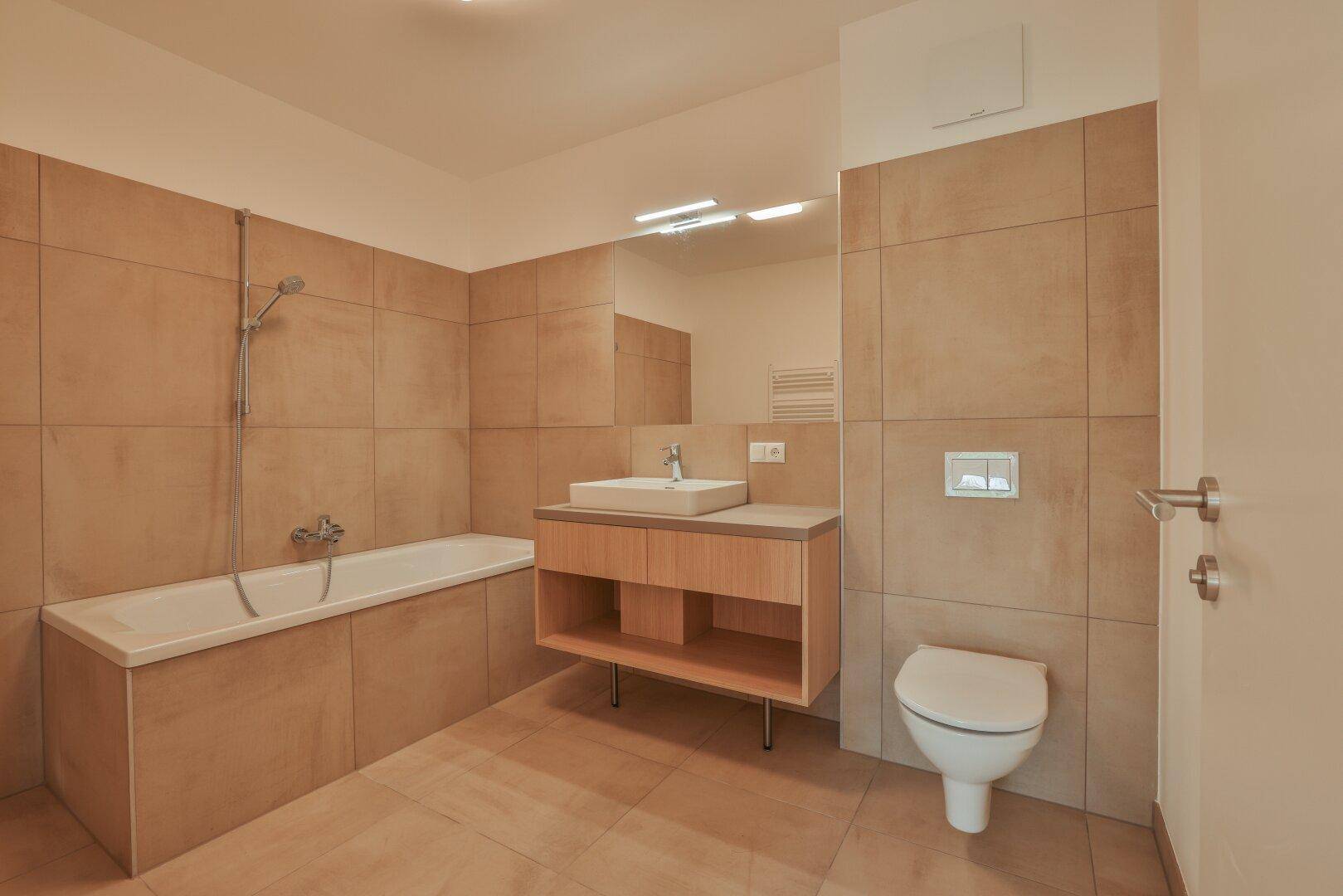 Modernes Badezimmer mit Badewanne, Waschtisch und Wand-WC, gefliest in warmen Erdtönen.