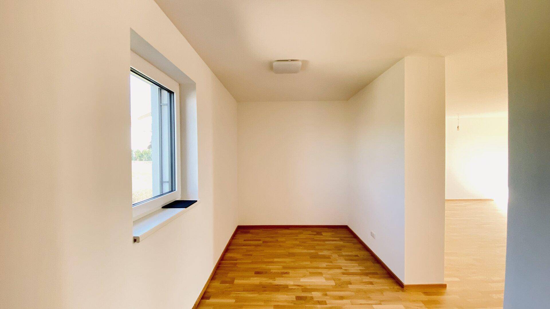 Heller, leerer Raum mit einem Fenster und hellem Parkettboden, bereit für die individuelle Gestaltung.