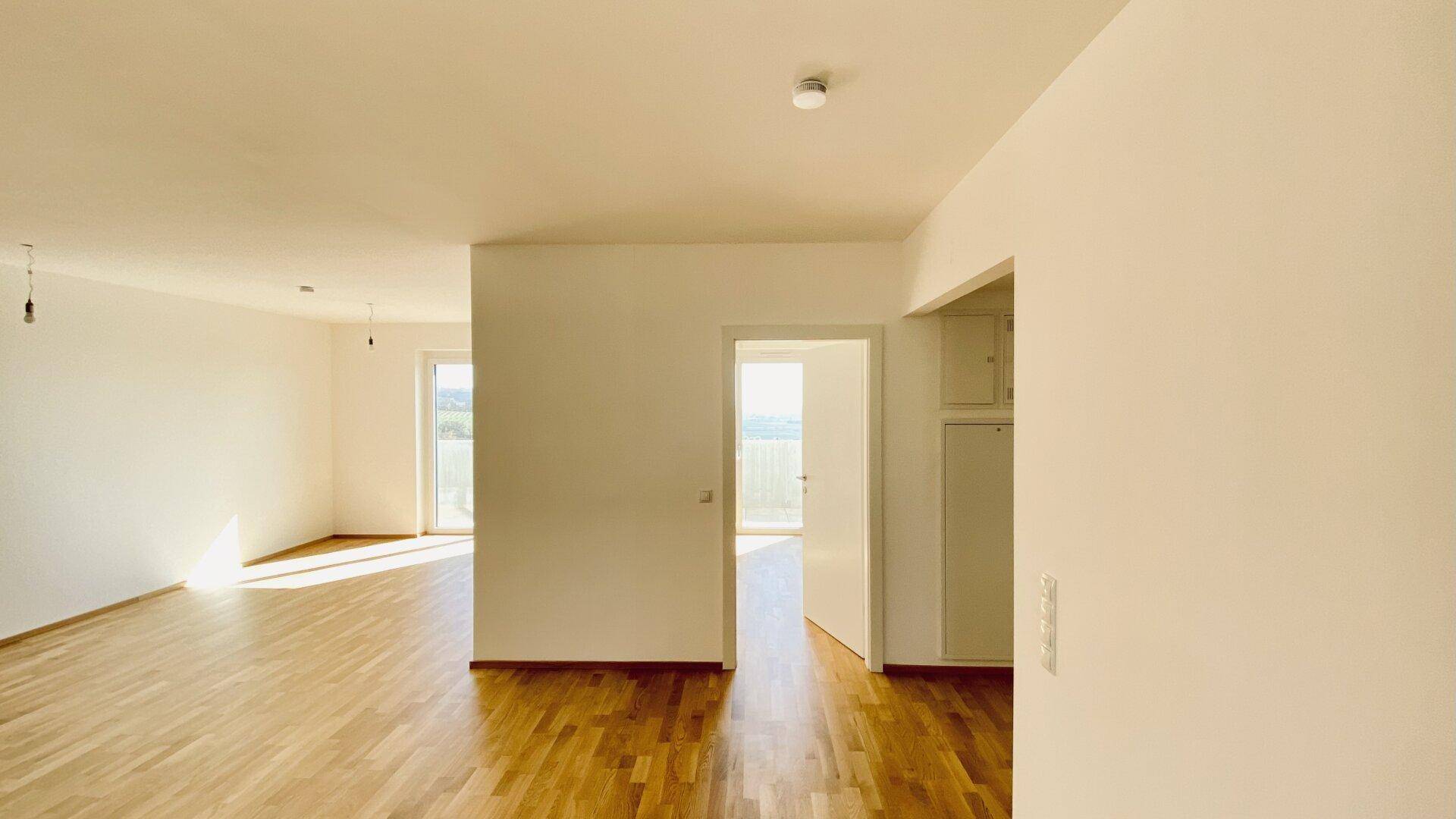 Geräumiger, heller Wohnbereich mit Holzboden und Zugang zu einem Balkon oder einer Terrasse.