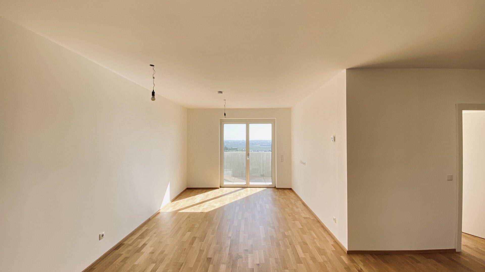 Lichtdurchfluteter Wohnbereich mit Holzboden und großen Schiebetüren, die zu einem Außenbereich führen.