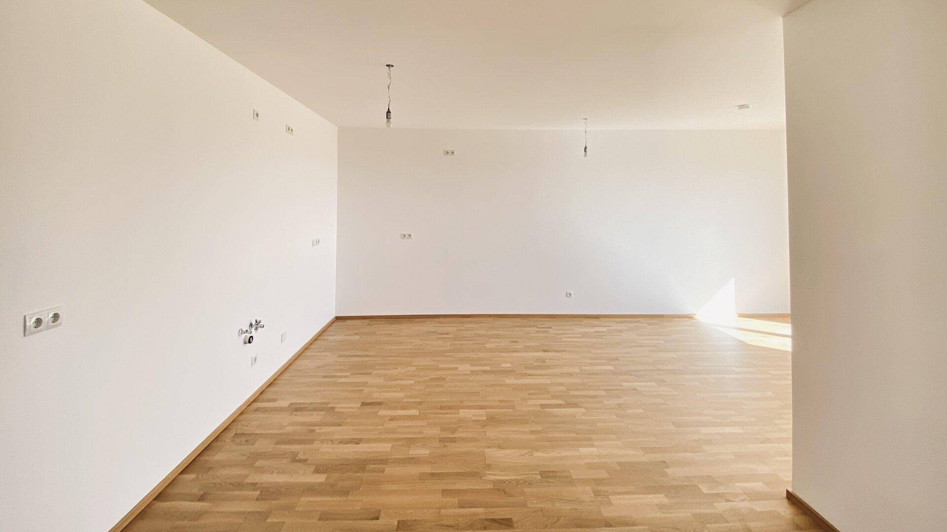 Großer, leerer Wohnraum mit hellem Parkettboden und weißen Wänden, ideal für offene Gestaltungskonzepte.