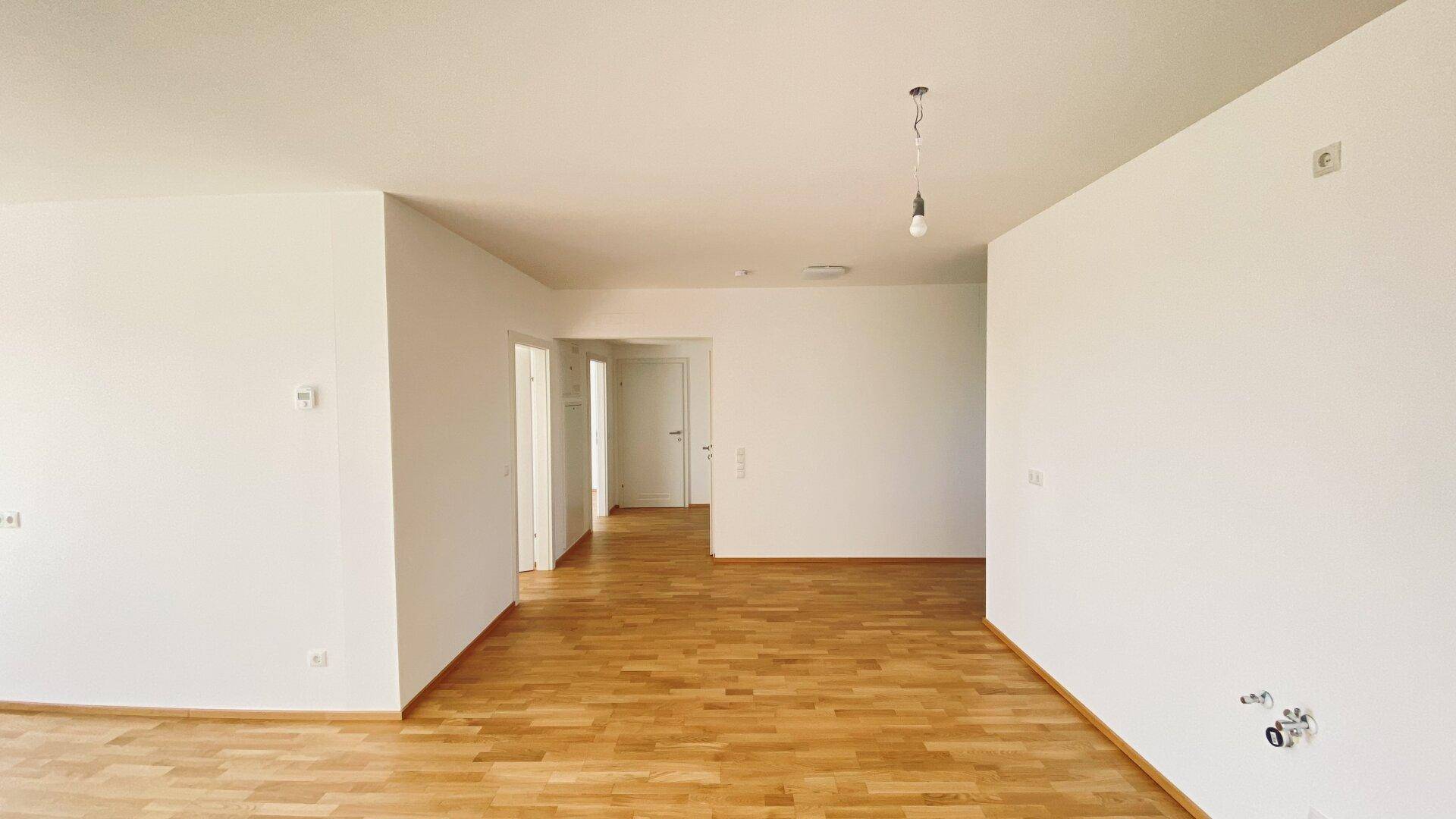 Heller Wohnraum mit Parkettboden und mehreren Türen, die zu angrenzenden Zimmern und einem Flur führen.