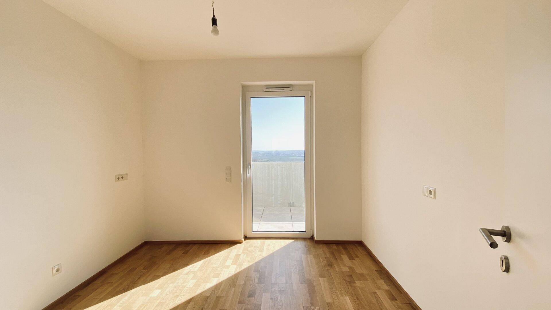 Helles Schlafzimmer mit Parkettboden und einer Tür, die zu einem privaten Balkon oder einer Terrasse führt.