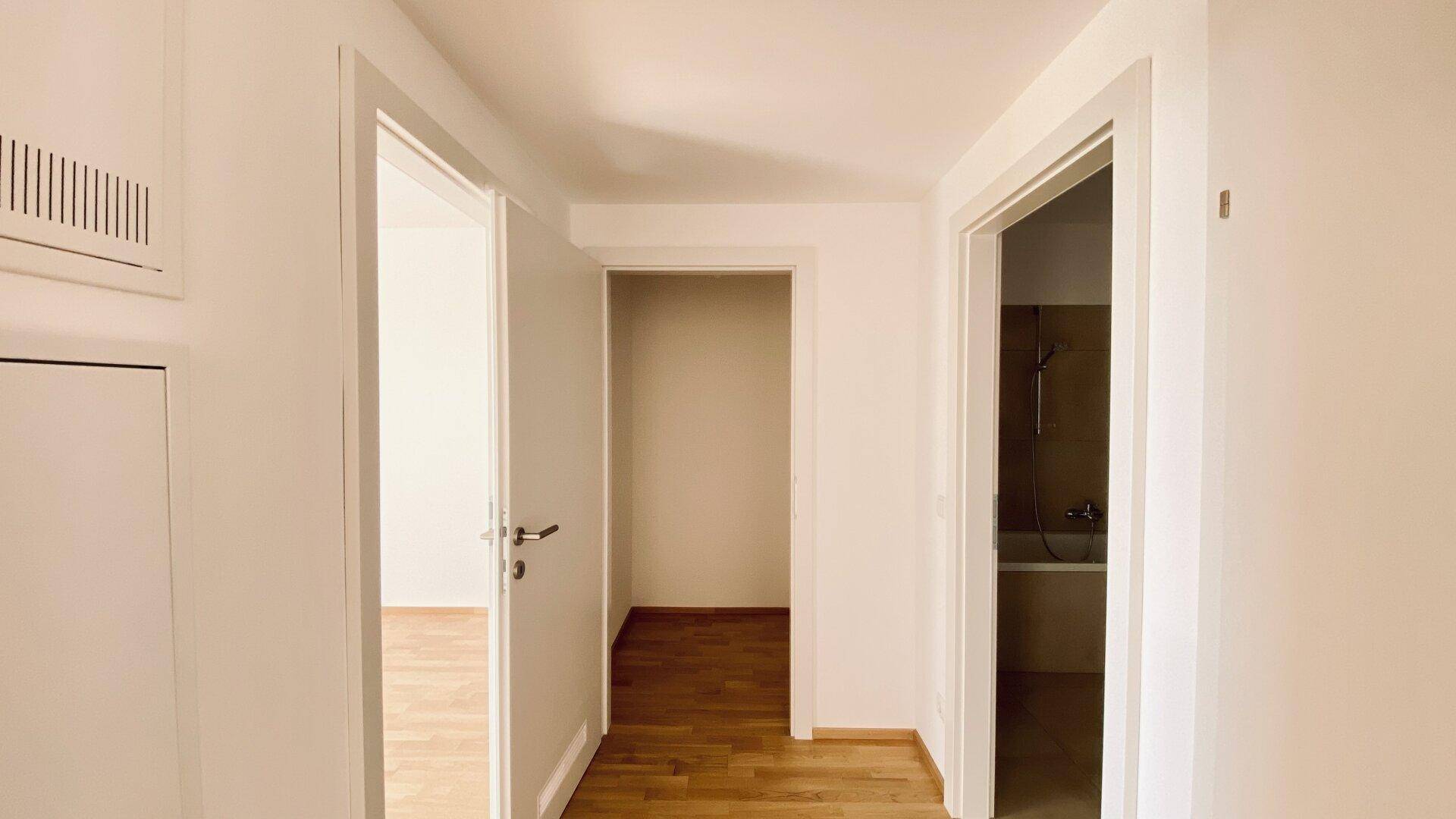Heller Flur mit Parkettboden und Türen, die zu verschiedenen Zimmern und einem Badezimmer führen.