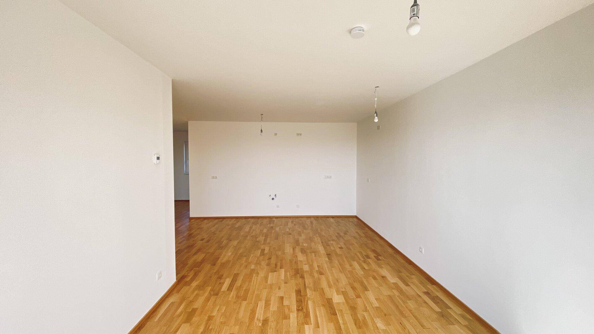 Großer, unmöblierter Wohnraum mit hellem Parkettboden und weißen Wänden, bereit zur individuellen Gestaltung.