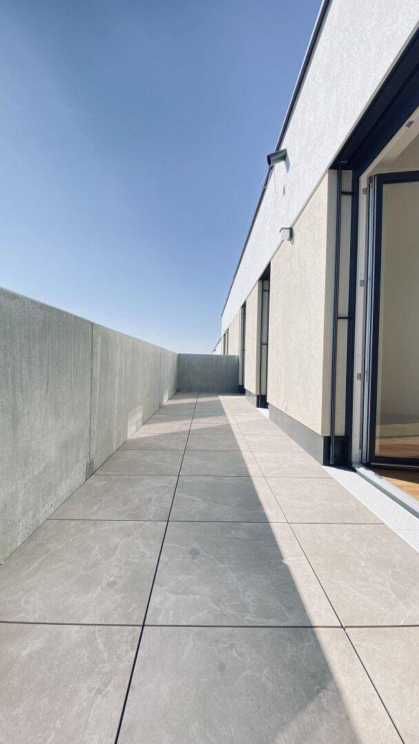 Lange, sonnige Terrasse mit modernen Fliesen und einer klaren Brüstung, die viel Platz bietet.