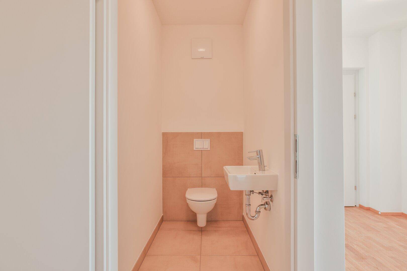 Kleines Gäste-WC mit Wand-WC, Handwaschbecken und beigefarbenen Fliesen im unteren Bereich.