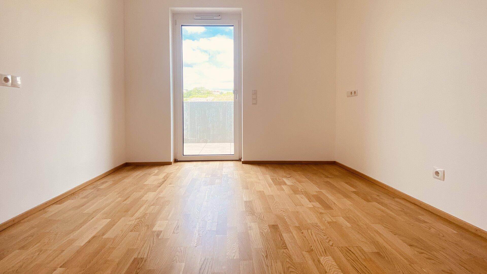 Helles Schlafzimmer mit Parkettboden und Zugang zu einem Balkon, das viel natürliches Licht erhält.