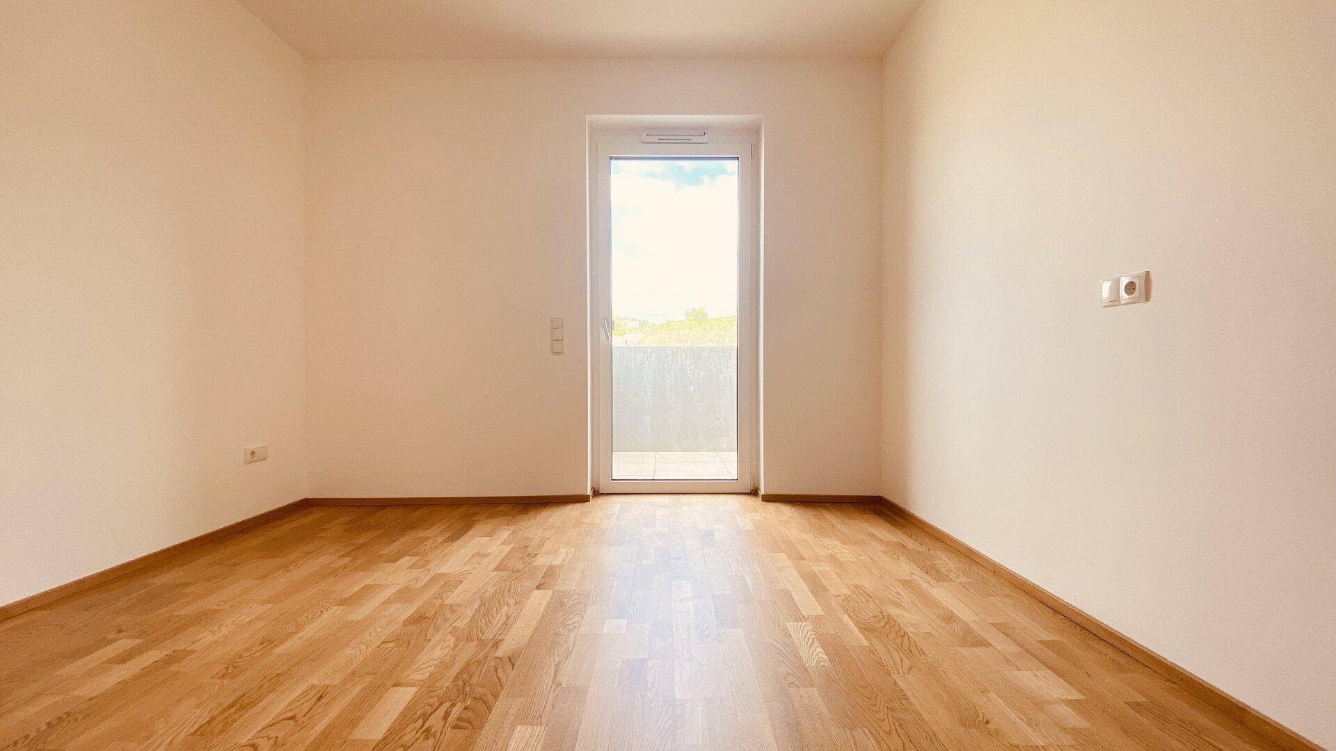 Geräumiges Schlafzimmer mit Parkettboden und Balkonzugang, das eine angenehme Wohnatmosphäre schafft.