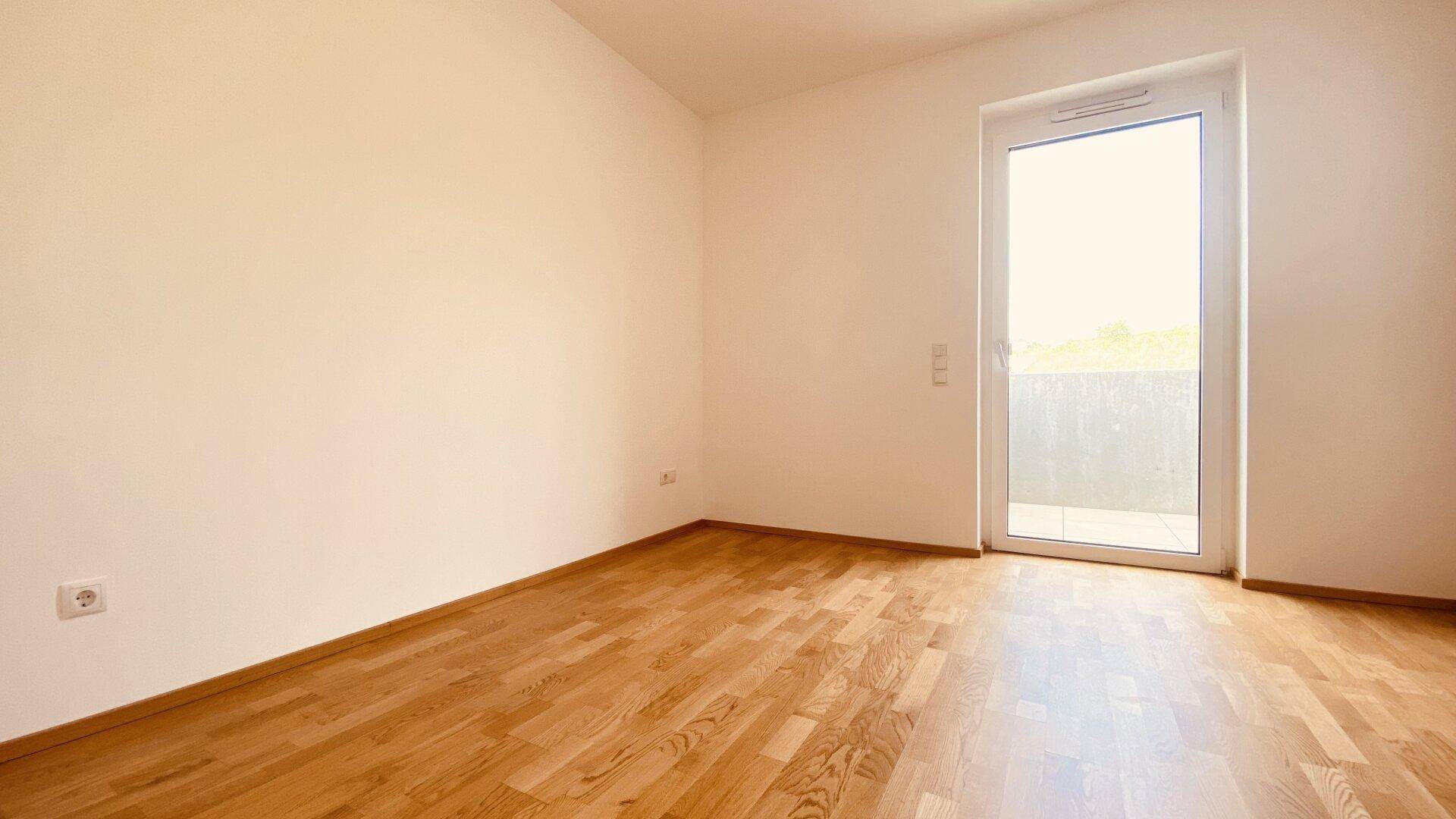 Ruhiges Schlafzimmer mit Parkettboden und Balkontür, ideal für erholsame Stunden.