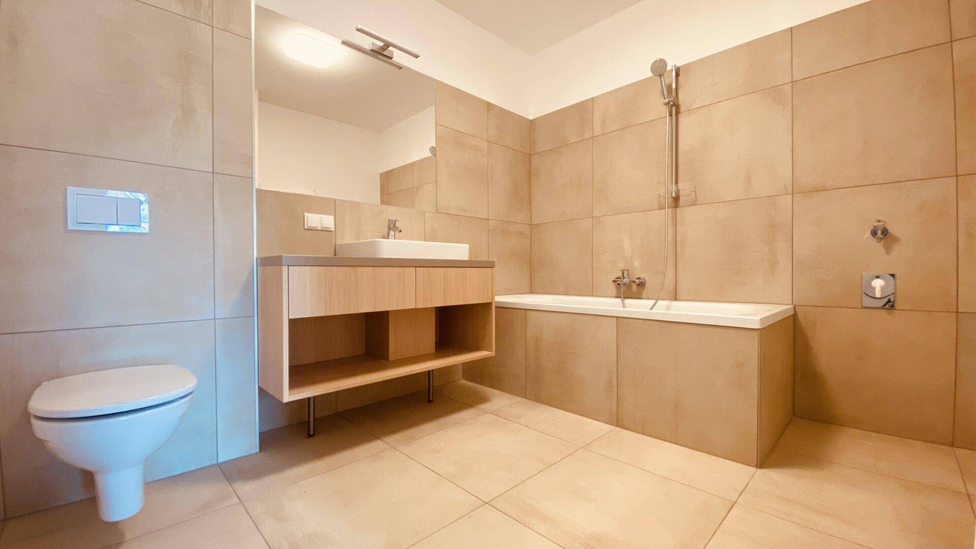 Modernes Badezimmer mit beigefarbenen Fliesen, Badewanne mit Duschfunktion und schwebendem Waschtisch.