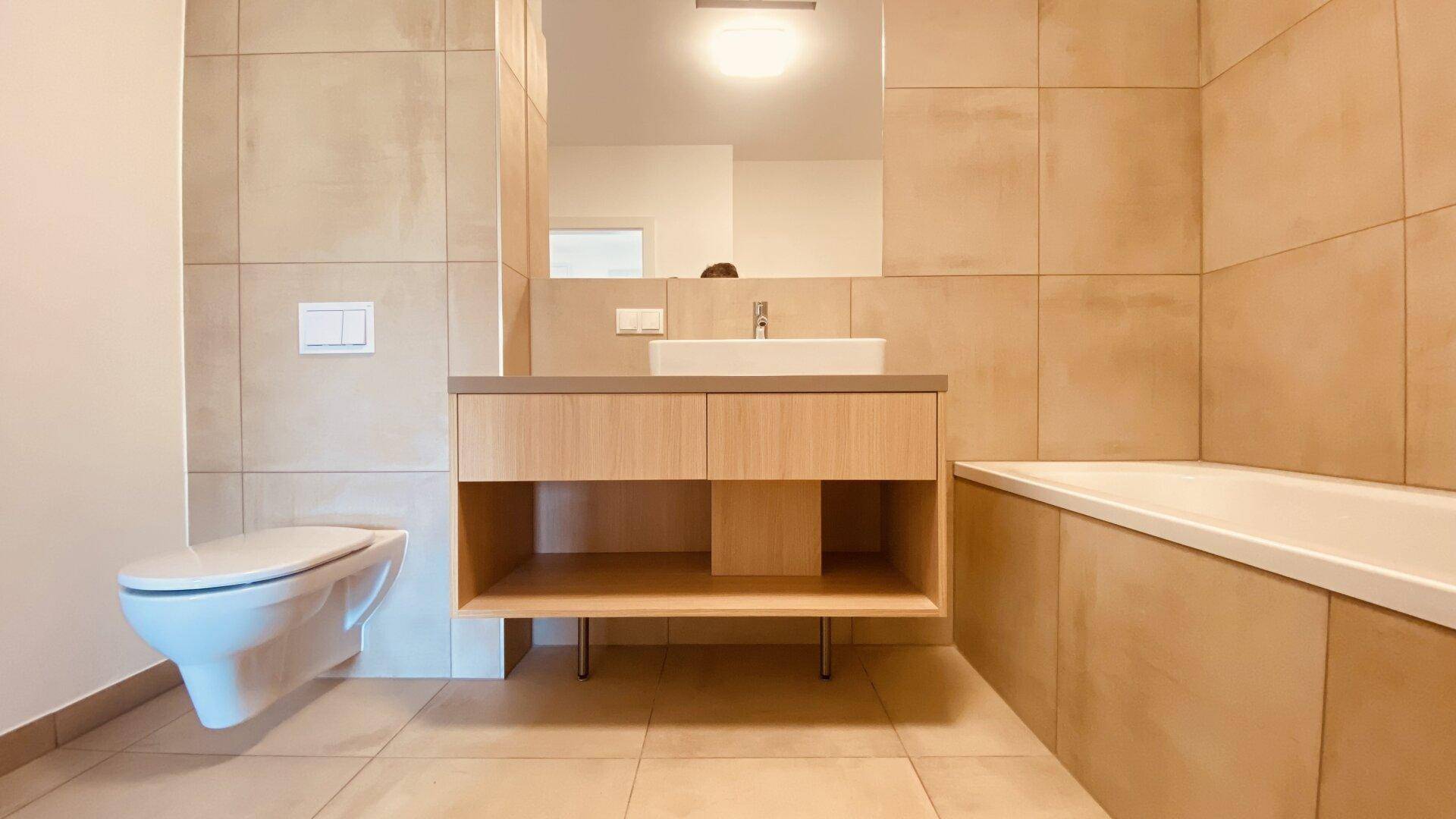 Stilvolles Badezimmer mit modernem Waschtisch, Wand-WC und großformatigen beigefarbenen Fliesen.