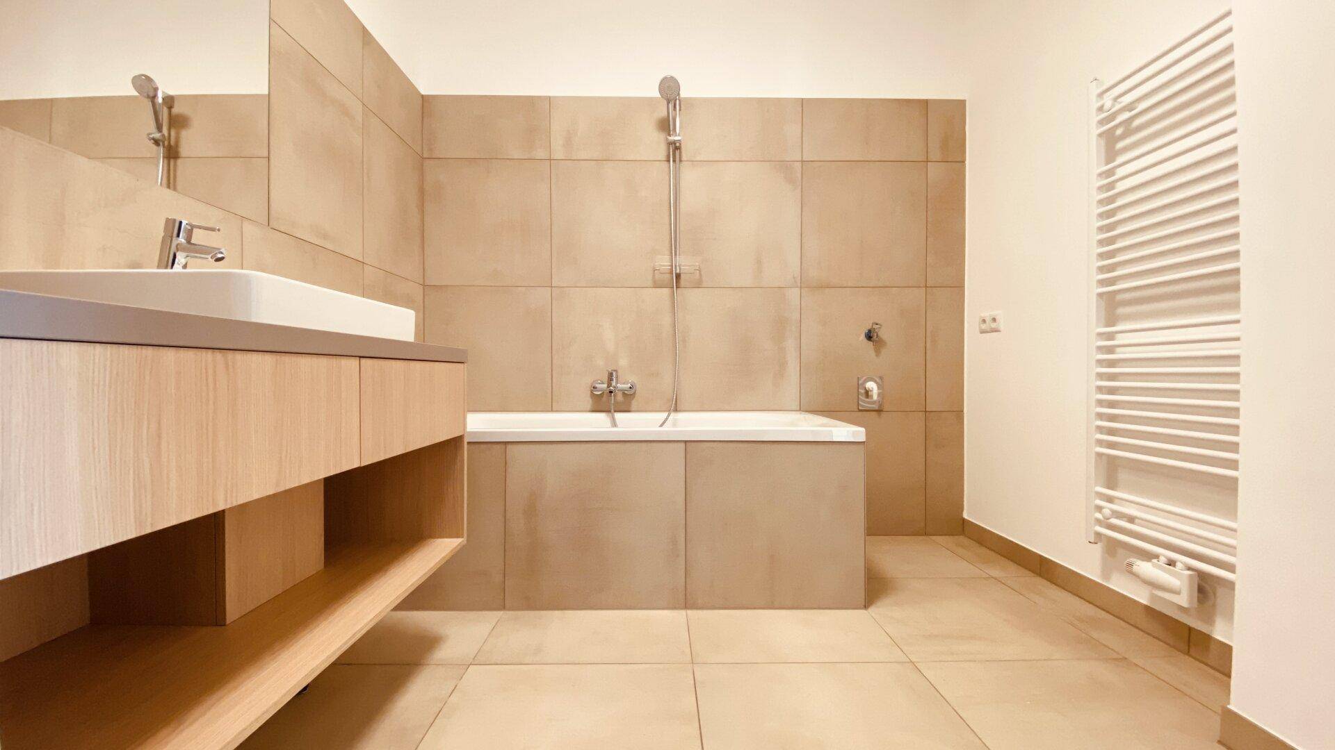 Helles Badezimmer mit Badewanne, beheiztem Handtuchhalter und modernen beigefarbenen Fliesen.