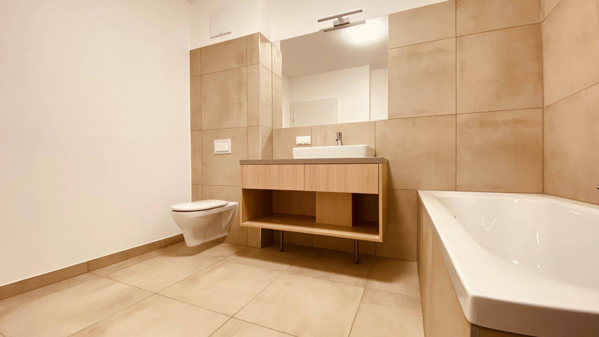 Geräumiges Badezimmer mit moderner Ausstattung, Badewanne und Waschtisch, alles in hellen Beigetönen gehalten.