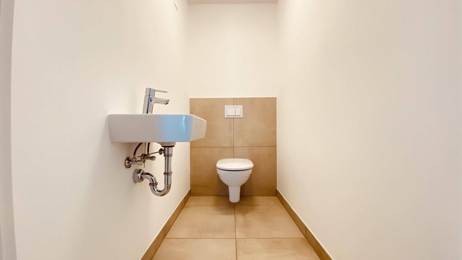 Modernes Gäste-WC mit kleinem Waschbecken und Wand-WC, ausgestattet mit hellen Fliesen.