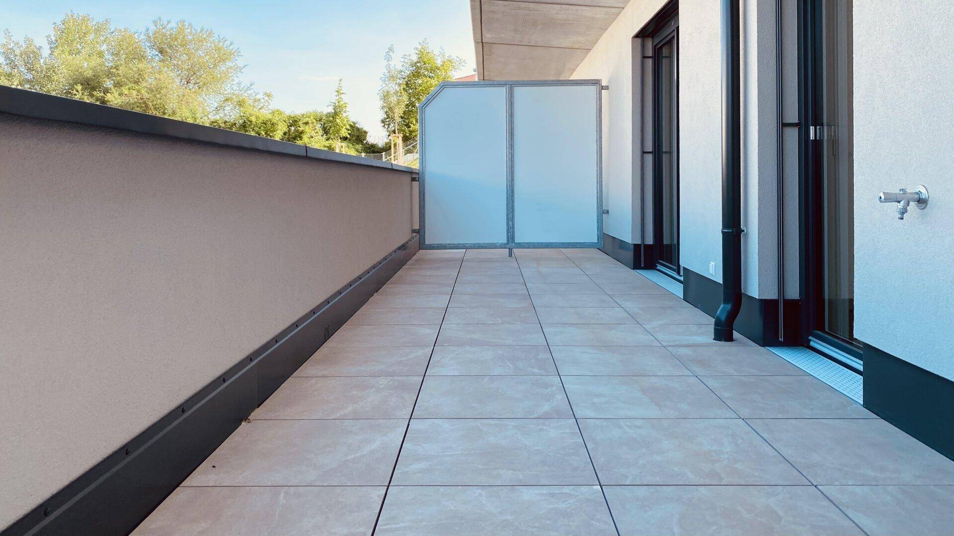 Langer, gefliester Balkon mit seitlichem Sichtschutz und Blick auf die Umgebung.